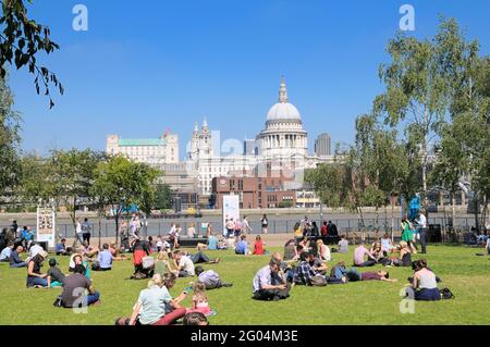 People relaxing on grass on a warm sunny day in Tate Modern gardens opposite St Paul's Cathedral, Bankside, South Bank, London, England, UK Stock Photo