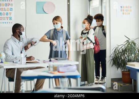 Portrait of male teacher wearing mask and greeting kids entering school classroom, covid safety measures Stock Photo