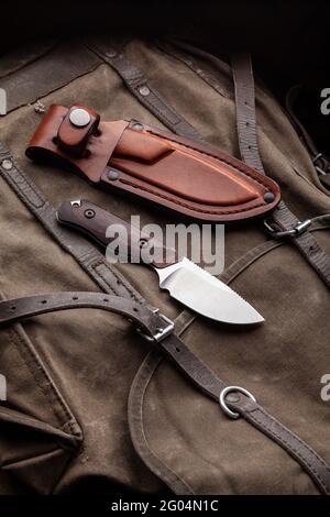 A hunting knife with a wooden handle and a leather case on a khaki canvas backpack. Weapons for self-defense and survival. Stock Photo