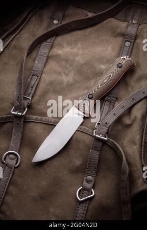 A hunting knife with a wooden handle on a khaki canvas backpack. Weapons for self-defense and survival. Stock Photo