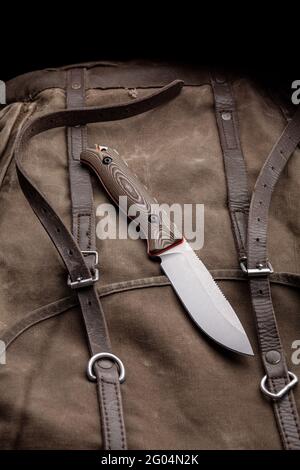 A hunting knife with a wooden handle on a khaki canvas backpack. Weapons for self-defense and survival. Stock Photo