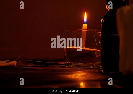 Burning candle on a table in a restaurant in a glass candlestick. Stock Photo