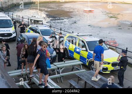man in blue top and base ball cap standing on garden table talking to policemen in face mask in front of marked police car, Margate, Kent, England Stock Photo