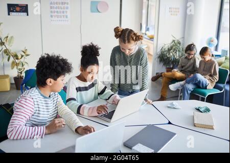 High angle view at diverse group of children working together at desk in classroom at modern school, copy space