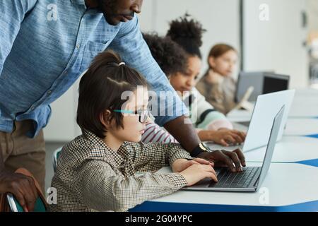 Side view portrait of young boy using computer in IT class with teacher helping him Stock Photo