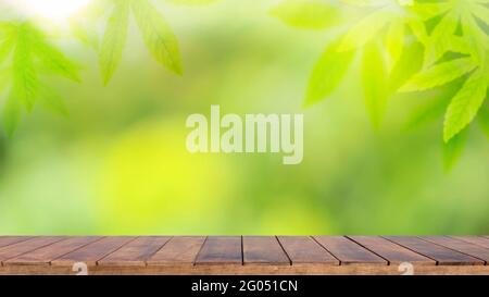 Wooden table background with cannabis leaf backdrop and blurred green nature backdrop for product display. Stock Photo