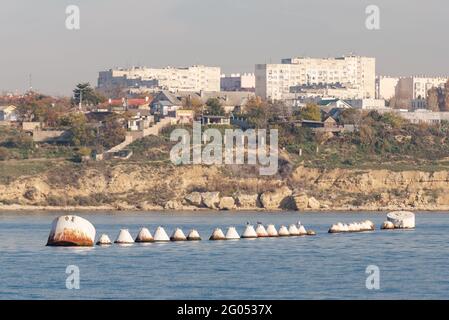 A row of large iron barrels for mooring ships. Buoys on the background of the city of Sevastopol inside the bay. Stock Photo