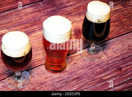 Three glass goblets with different types of dark beer stand on a wooden table. View from above. Stock Photo