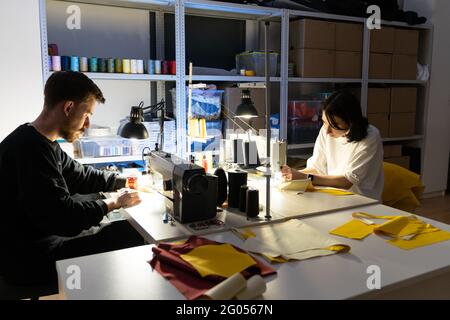 Two tailors sew on sewing machines in atelier. Team of clothes designers entrepreneurs work together Stock Photo
