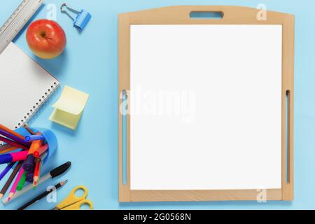 Flat lay with school concept on blue background with various schooling accessories, pens, pencil, notepad, paper clips, apple, ruler, scissors, empty Stock Photo