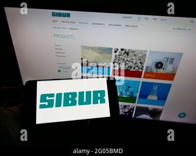 Person holding cellphone with logo of Russian petrochemicals company SIBUR Holding PJSC on screen in front of webpage. Focus on phone display. Stock Photo