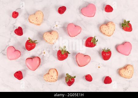 Heart shaped pink and beige French macaron sweets next to strawberry and raspberry fruits Stock Photo