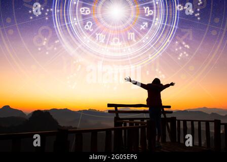 Woman raising hands looking at the sky. Astrological wheel projection, choose a zodiac sign. Trust horoscope future predictions, consulting stars. Stock Photo