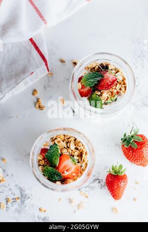 Two jars with tasty parfaits made of granola, strawberries and yogurt on marble table, top view Stock Photo