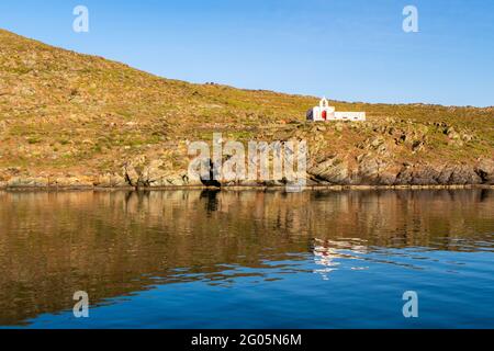 Old white abandoned Church Agios Ioannis on dramatic cliff on Kithnos Island, Greece, seen from the sea with beautiful reflection in calm water. Stock Photo