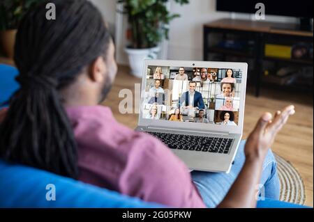 Group of diverse colleagues talks via video call. African-American man with locks hairstyle using laptop computer for virtual meeting with coworkers, business partners, peoples talk on the screen Stock Photo