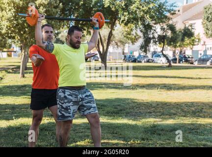 Personal trainer helping a man to do weights in a park on a sunny day. Stock Photo