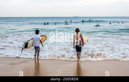 Rear view of two surfers with surfboards walking out to sea, Hikkaduwa, Southern Province, Sri lanka Stock Photo