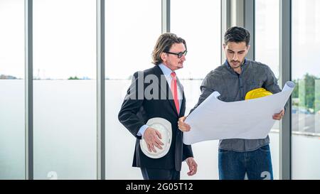 Two Caucasian engineer teamwork standing meeting and looking to paperwork for planning project. Professional corporation people. Stock Photo