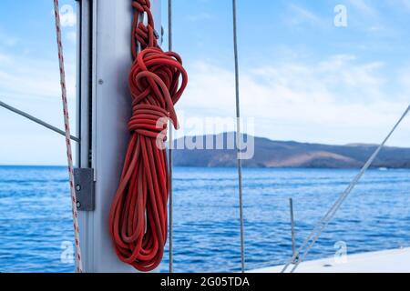 Mooring ropes on the sailing boat, blur seascape background. Red color yachting rope on the ship mast. Closeup view, copy space. Sailboat cruise card Stock Photo