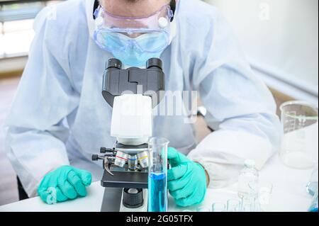Male scientist wearing protection suit working with  microscope and many lab equipment for research at laboratory. Medical researcher specialist. Stock Photo