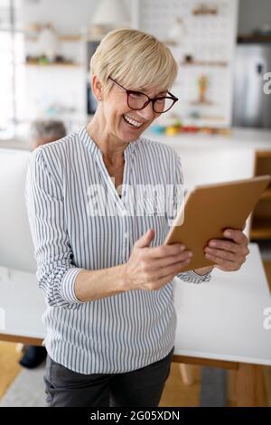 Beautiful happy senior woman using tablet computer at home Stock Photo