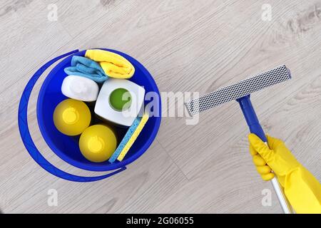 Detergents in plastic bottles, sponges in blue household bucket. Mop for washing windows in hand in yellow rubber glove Сleaning accessories. Flat lay Stock Photo