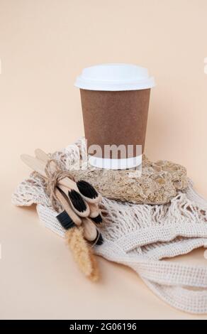 Brown sustainable paper coffee cup, reusable shopping bag and wooden toothbrush on a natural stone on a beige background Zero waste concept. Stock Photo