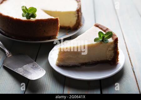 Plane round classic New York cheesecake and his slice with sprig of mint on a plate on a wooden table. The concept of bakery and sweet cakes desserts