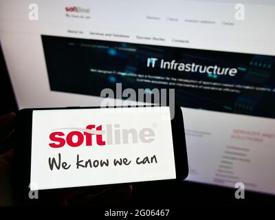 Person holding mobile phone with logo of global IT solutions provider Softline International on screen in front of web page. Focus on phone display. Stock Photo