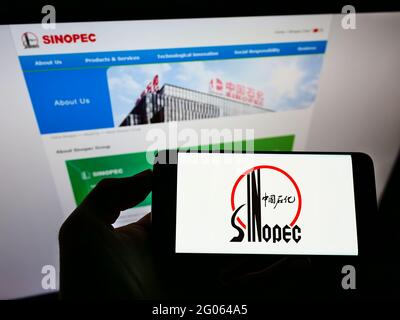 Person holding smartphone with logo of company China Petrochemical Corporation (Sinopec) on screen in front of website. Focus on phone display. Stock Photo