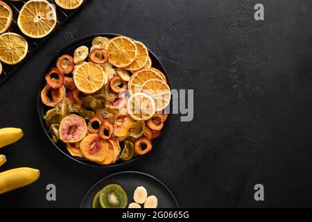 Dried different fruits sliced plums, kiwi, peach chipson black background, home drying. Snack vegan sugar free food. View from above. Copy space. Stock Photo