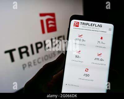 Person holding cellphone with webpage of Canadian company Triple Flag Precious Metals Corp. on screen with logo. Focus on center of phone display. Stock Photo