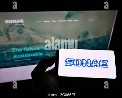 Person holding smartphone with logo of Portuguese conglomerate Sonae SGPS S.A. on screen in front of website. Focus on phone display. Stock Photo