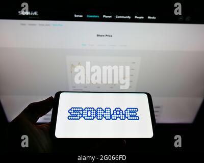Person holding mobile phone with logo of Portuguese conglomerate Sonae SGPS S.A. on screen in front of business website. Focus on phone display. Stock Photo