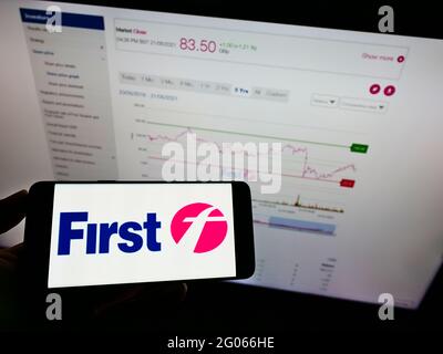 Person holding smartphone with logo of British transport company FirstGroup plc on screen in front of website. Focus on phone display. Stock Photo