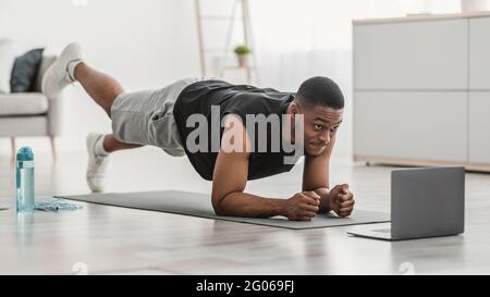 Man At Laptop Standing In Plank Doing Leg Raise Indoor Stock Photo