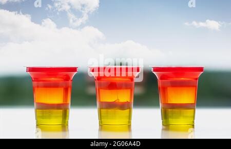 Three glasses of colorful striped jelly on a natural background. Rainbow jelly for kids party. Close up. Stock Photo