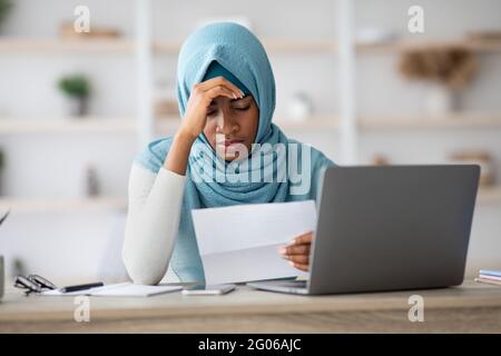 Stressed Black Muslim Woman Working With Papers And Laptop In Office Stock Photo