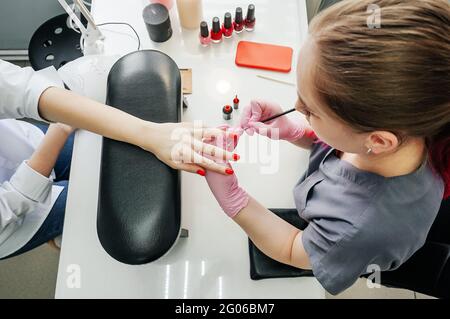 Young woman getting manicure in beauty salon. Manicurist make red manicure. Top view. Stock Photo