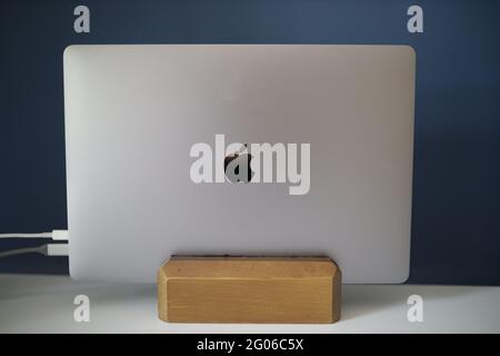 BRCKO DISTRIC, BOSNIA AND HERZEGOVINA - May 01, 2021: Space grey Apple MacBook Pro 16 inch on wooden vertical laptop stand, connected to power and ext Stock Photo
