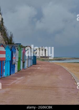 Stone Bay’s sweeping curved path, with its cliffs, sands and brightly coloured beach huts, under a heavy, clouded sky. Stock Photo