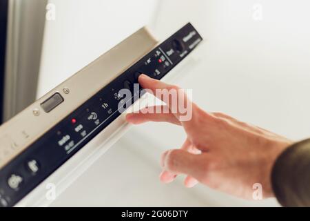 Man choosing mode on the control panel of the dishwasher. Stock Photo