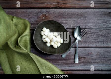 Fresh uncooked gnocchi in a green ceramic bowl, vintage cutlery, on a printed tablecloth, Italy, Europe Stock Photo