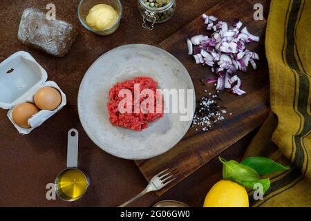 Ingredients for the preparation of beef tartare on an old wooden cutting board, kitchen fabric and rusty metal background, flat lay, Italy, Europe Stock Photo