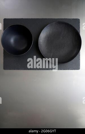 Black ceramic plate and bowl on a slate stone and metallic background with space for text Stock Photo