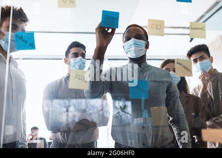 Colleagues in face masks having meeting using sticky notes Stock Photo
