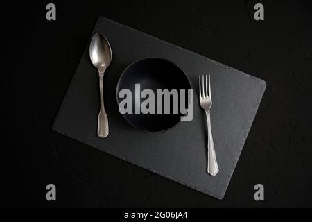 Empty black ceramic bowl, vintage cutlery over a dark slate background Stock Photo