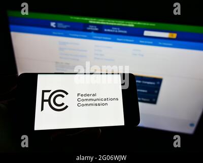 Person holding cellpohone with seal of American agency Federal Communications Commission (FCC) on screen in front of website. Focus on phone display. Stock Photo