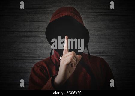an unknown person without a face in a hood shows a finger gesture meaning towns. The concept of anonymity and secrecy in the network. Stock Photo